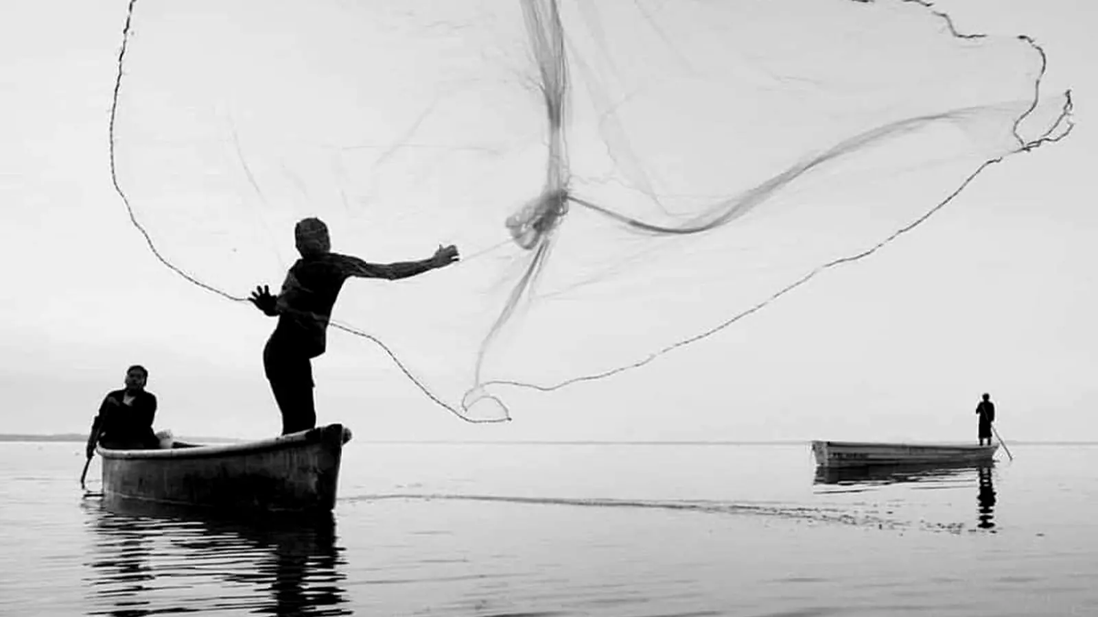 A fisherman casting a net from a boat on still water